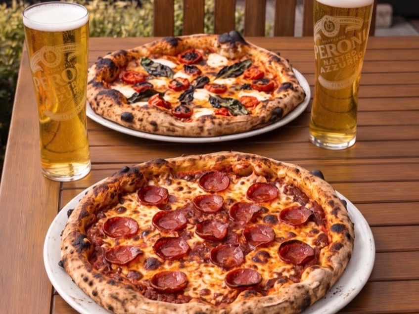Two stone-baked pizzas and two pints on a garden table
